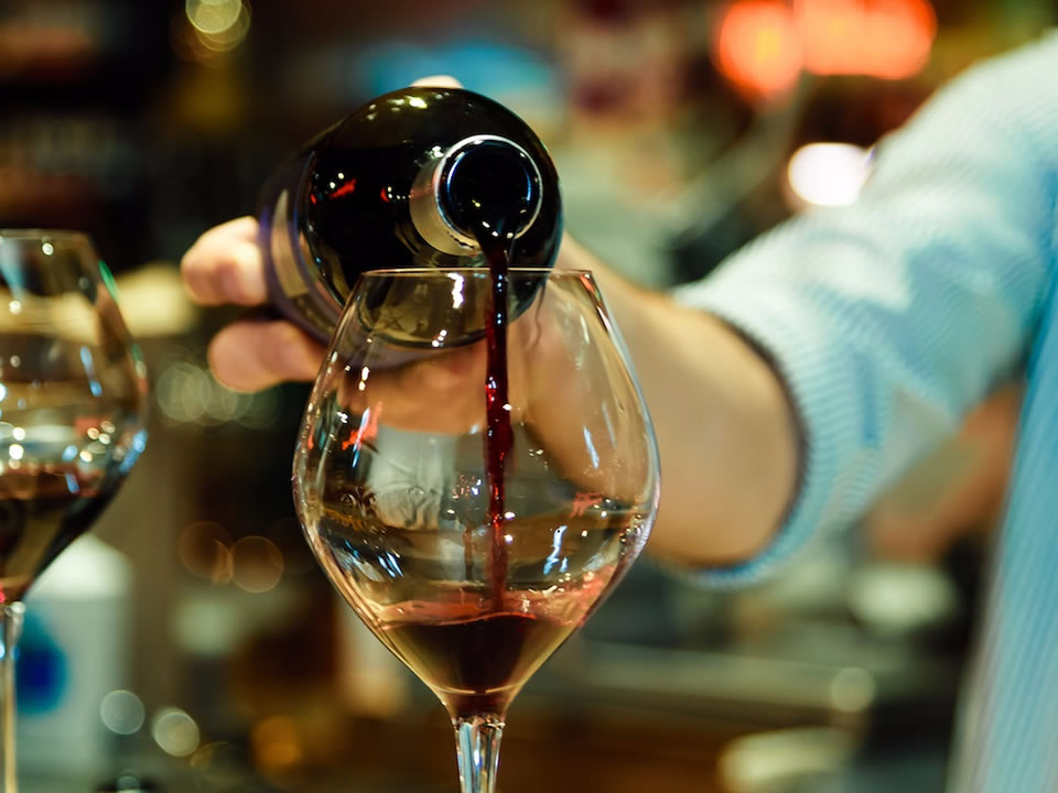 Red wine being poured into a wine glass by a bartender